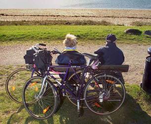 To fritidscyklister, der holder pause på en bænk og nyder udsigten ud over havet. 